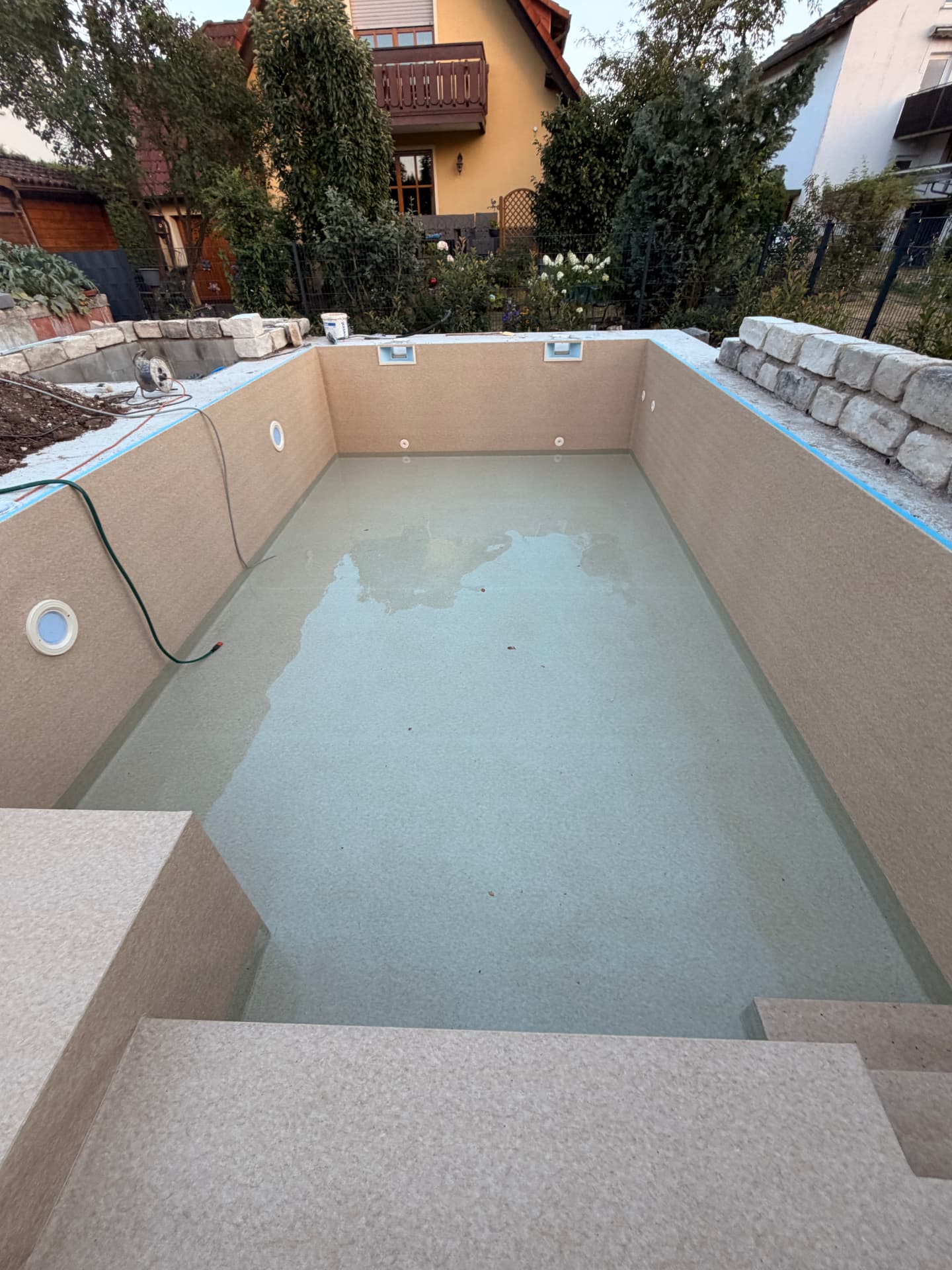 Mit beiger Folie ausgekleideter Pool mit Treppe bei der Erstbefüllung